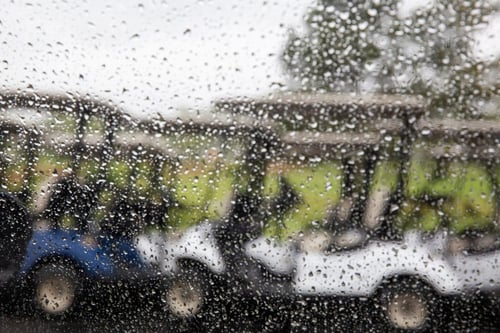 a POV shot looking through a rain-soaked windshield. Beyond the windshield, you can see a row of golf carts.