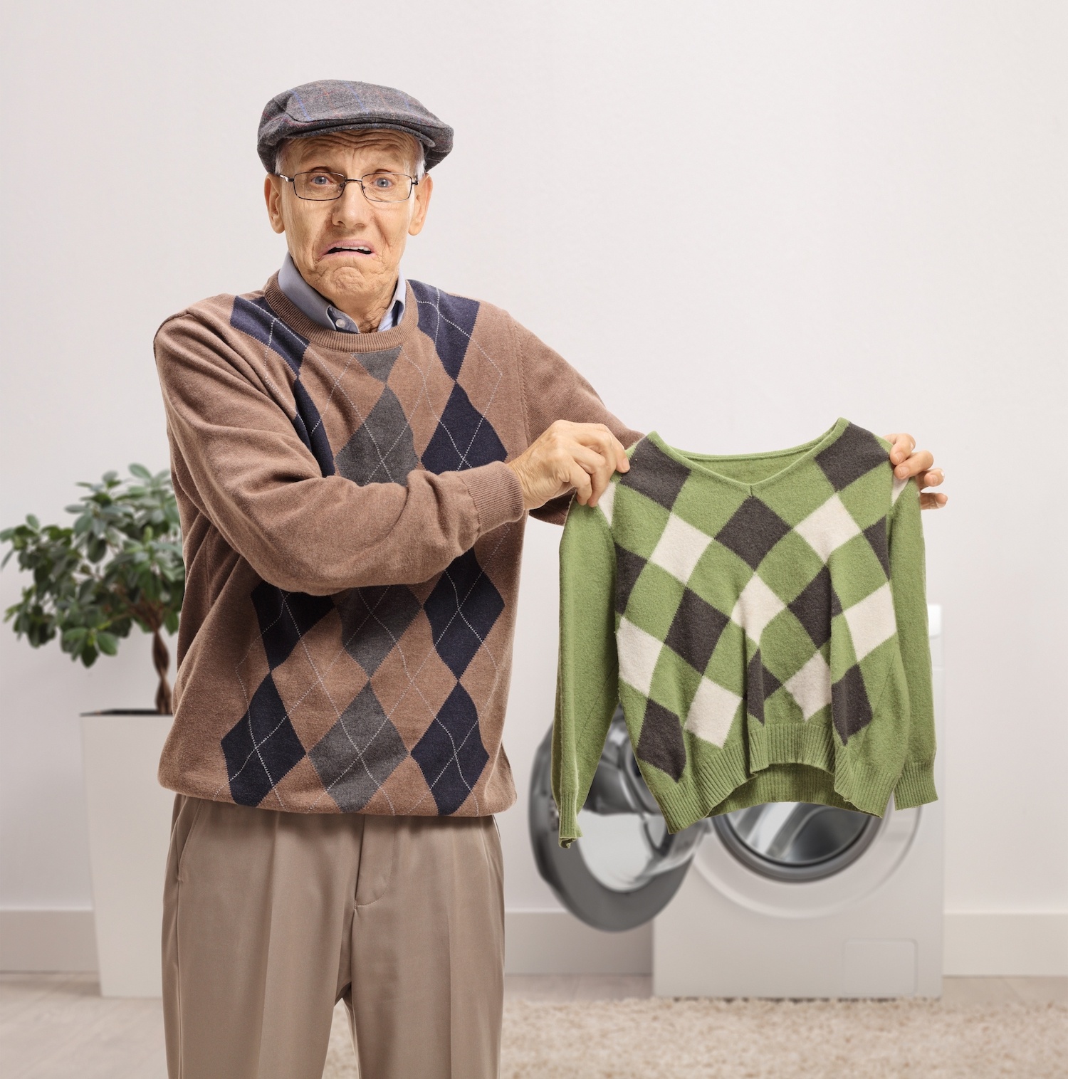 Disappointed senior man holding a shrunken blouse inside a bathroom