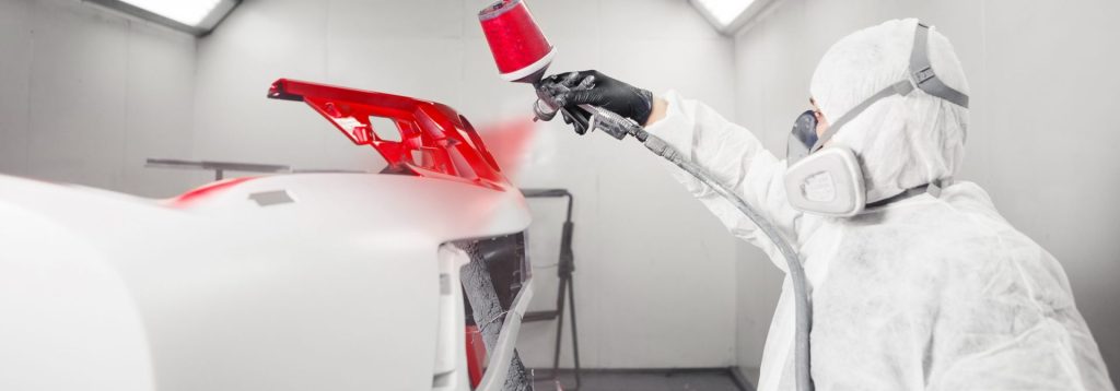 worker spray painting plastic piece on a car